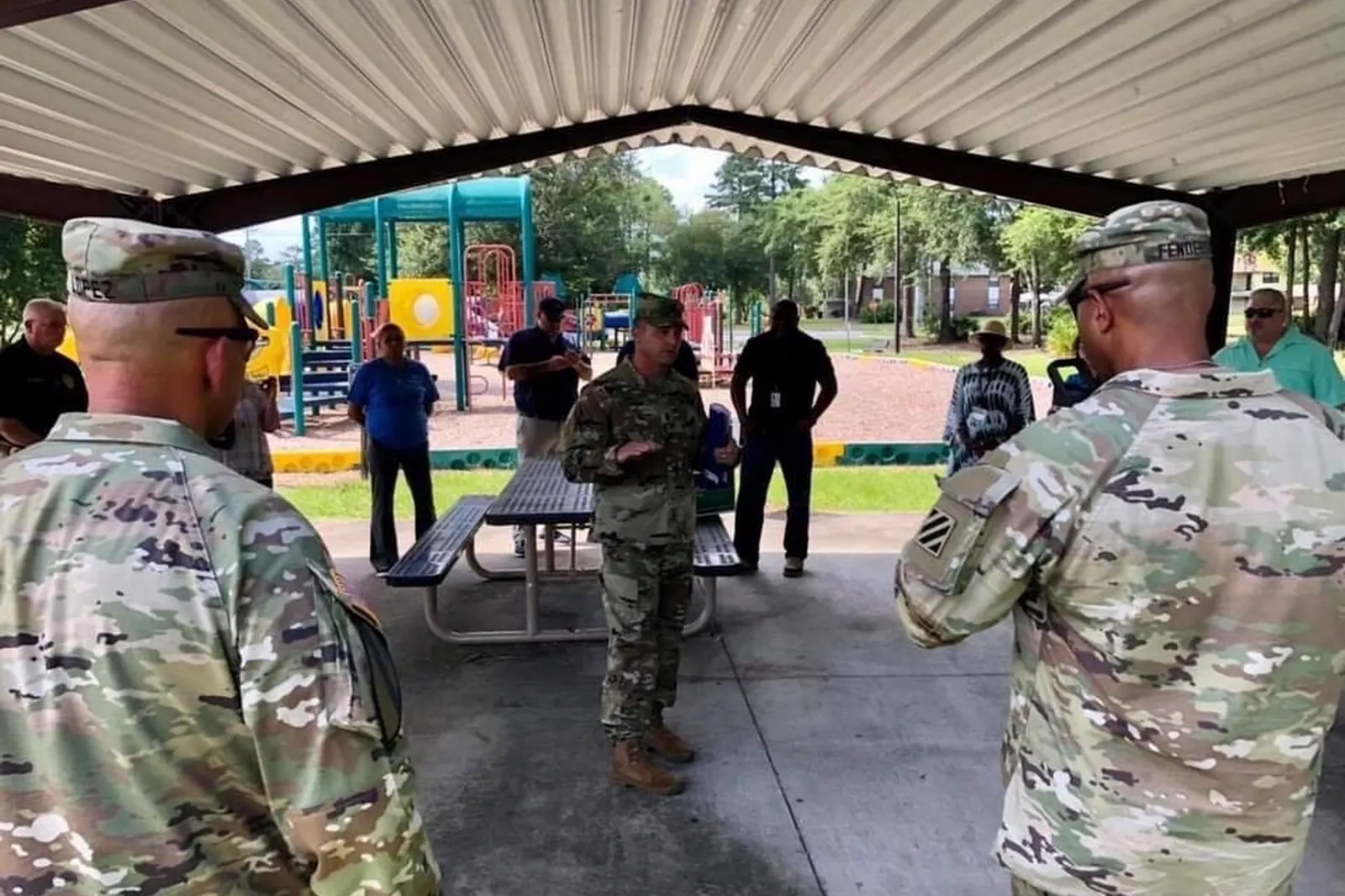 Leaders and housing staff under a picnic pavilion beside a neighborhood playground in Bryan Village