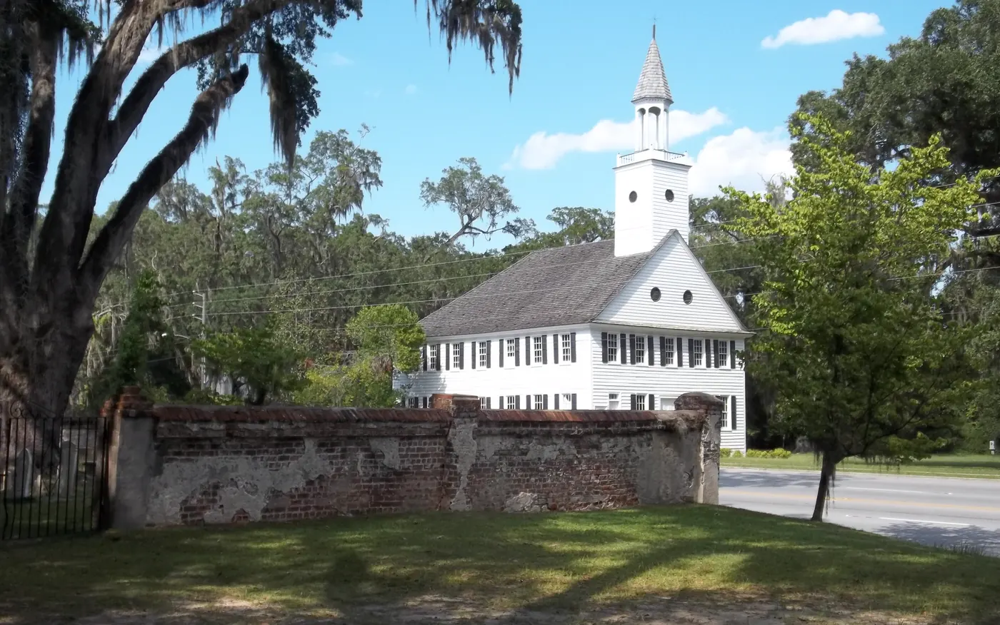 Historic Midway Congregational Church, white with a tall steeple, behind the old brick cemetery wall and framed by a live oak